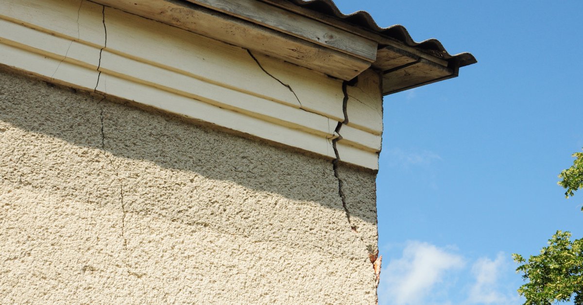 The corner of a home that has large cracks forming directly underneath the roof, going all the way through the wall.