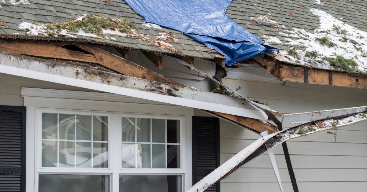 The roof of a home with major damage. There is a large crack in the roof and the gutter is detached from the roof.
